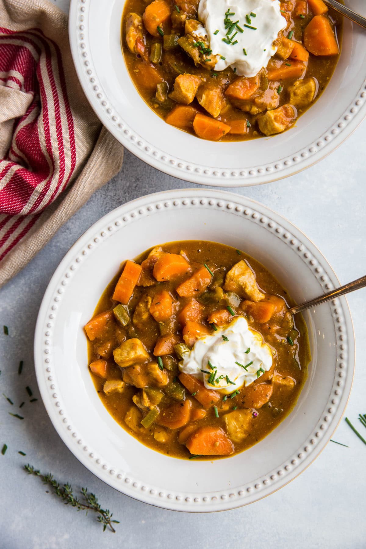 Two white bowls full of pumpkin chili with fresh herbs to the side and a rustic napkin.