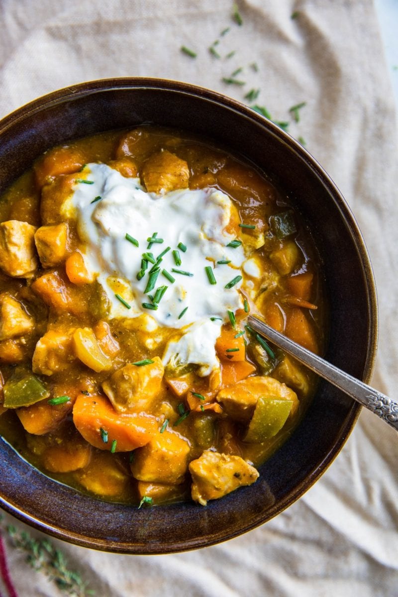 Large blue ceramic bowl full of paleo chicken chili with a spoon and a napkin, ready to serve.