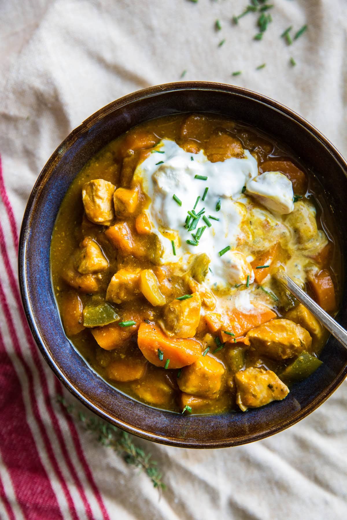 Blue ceramic bowl full of pumpkin chicken chili with a napkin underneath it and fresh herbs to the side.