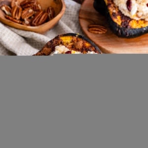 Acorn Squash stuffed with quinoa, pecans, goat cheese, dried cranberries sitting on a wooden plate.