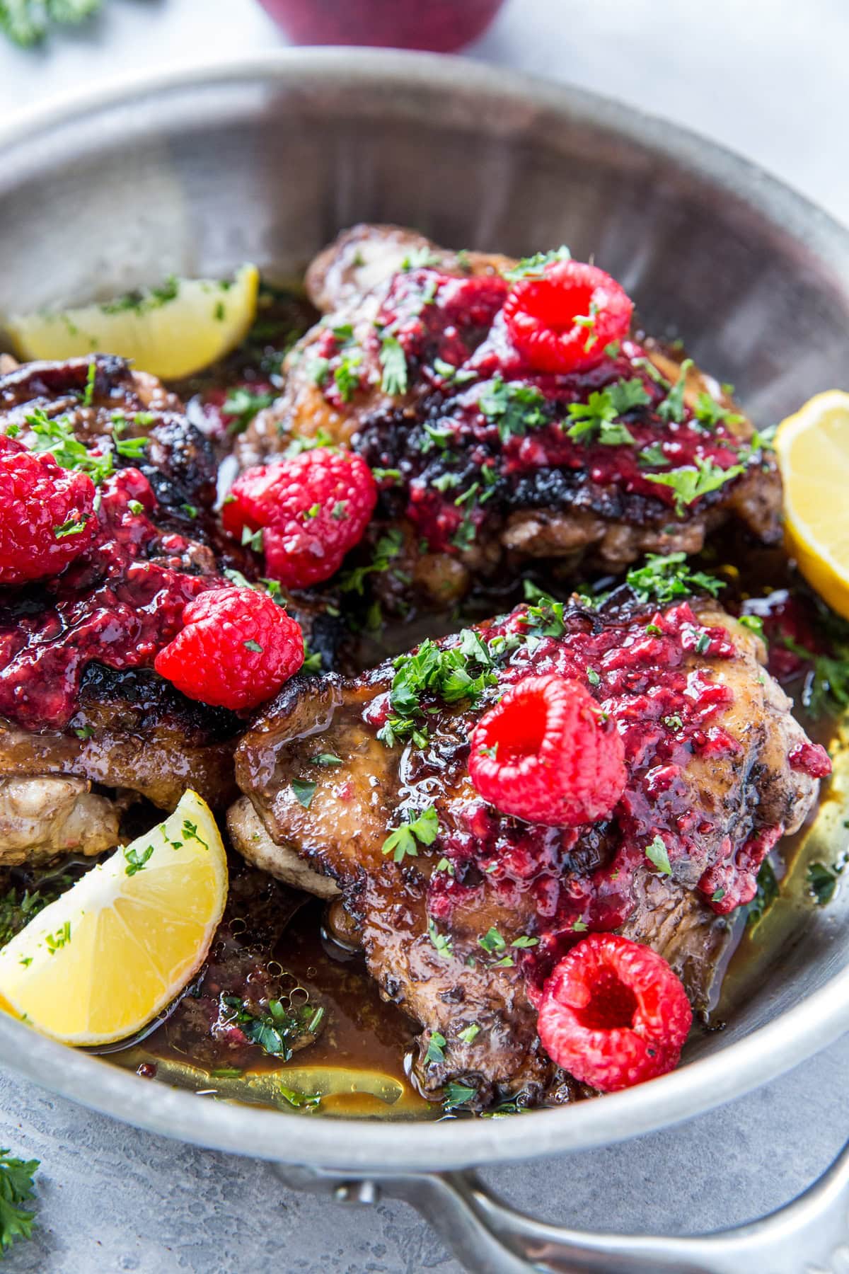 Stainless steel skillet full of golden brown chicken thighs with balsamic vinegar and raspberry jam on top, ready to serve.