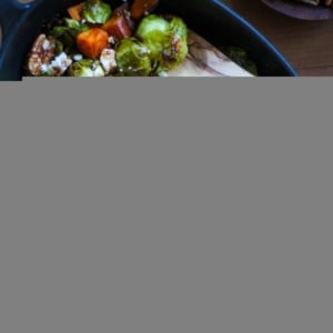 large cast iron baking dish filled with roasted brussels sprouts, sweet potatoes, pecans, feta cheese, and a balsamic drizzle. Ready to serve.