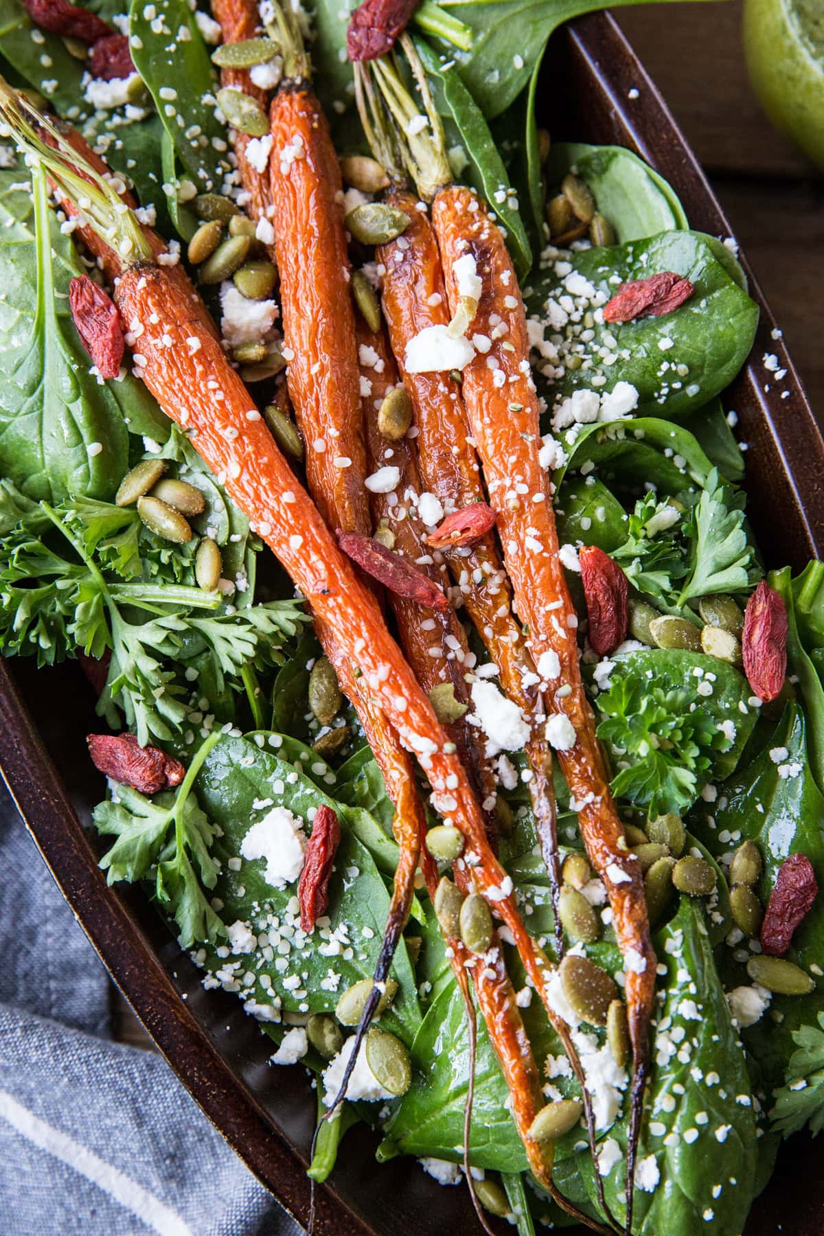 Roasted Carrot Spinach Salad with Lemon Herb Dressing in a large serving bowl. Roasted pumpkin seeds, feta cheese, and goji berries sprinkled on top