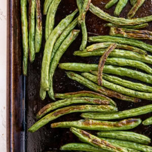 Roasted green beans on a large baking sheet fresh out of the oven with golden brown color.
