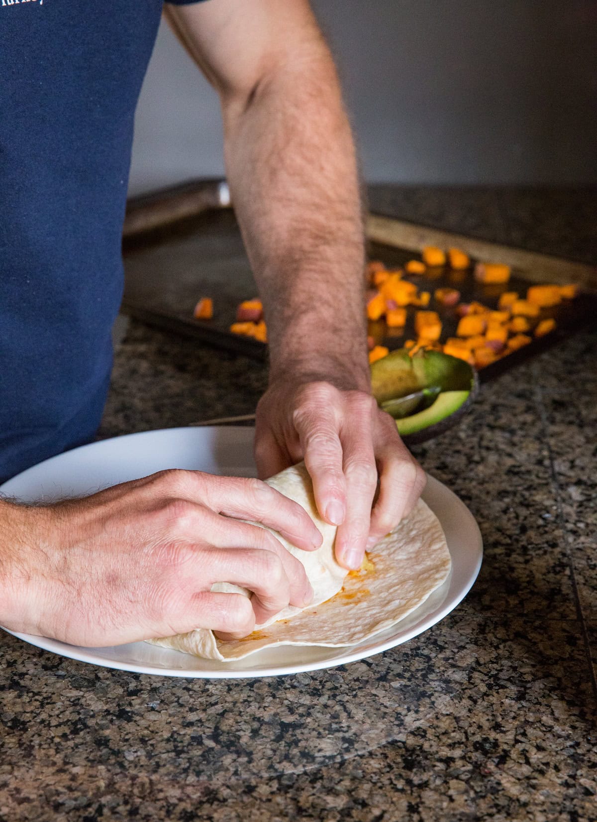 Man folding a breakfast burrito on a plate.