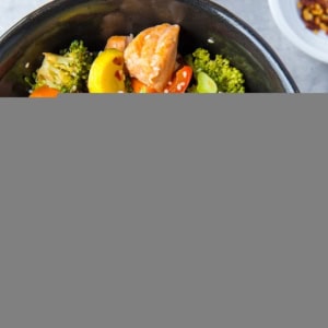 Black bowl of stir fry salmon and vegetables with chopsticks to the side and a dark blue napkin, ready to consume.