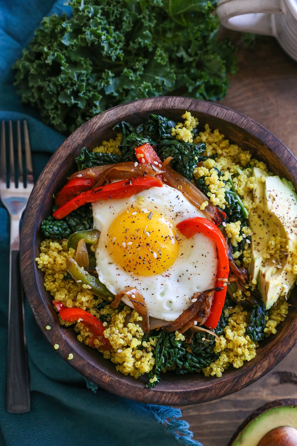 Quinoa, peppers, kale, and eggs in a wooden bowl.