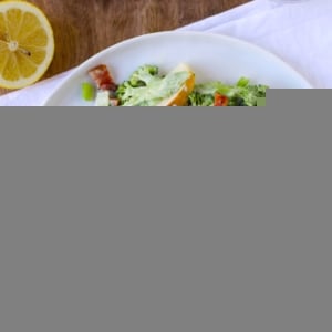 Shaved broccoli on a plate with bacon, apples and a glass of wine to the side. A napkin underneath the plate of salad.
