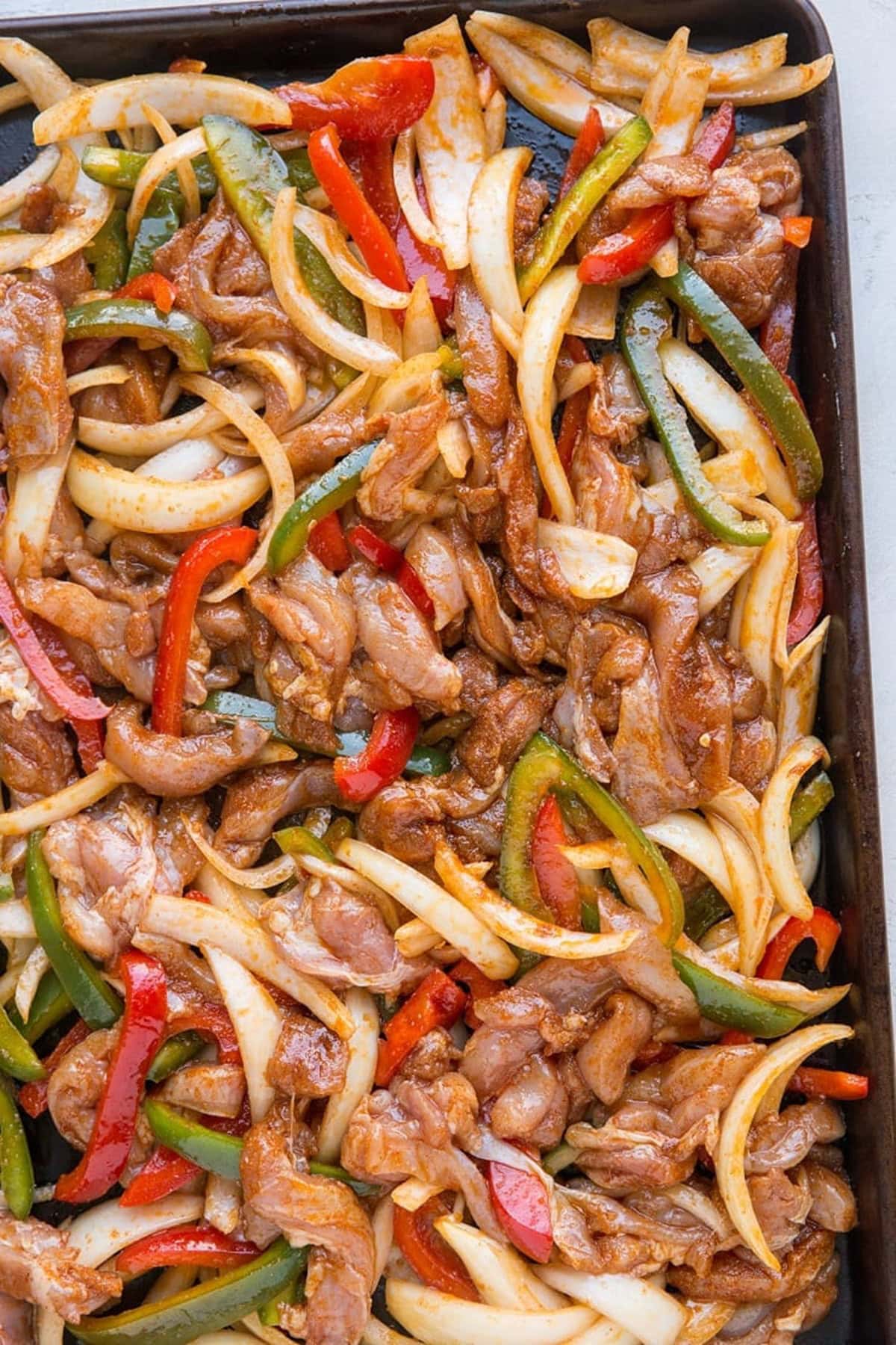 Ingredients for chicken fajitas on a baking sheet, ready to go into the oven.