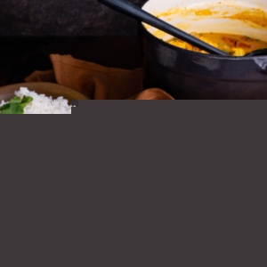 Shrimp curry in a brown ceramic bowl with the pot of the rest of the curry in the background.
