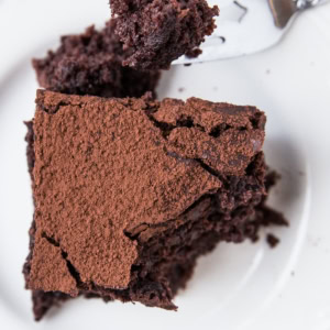 Slice of sourdough chocolate cake on a white plate with a fork taking a bite out.