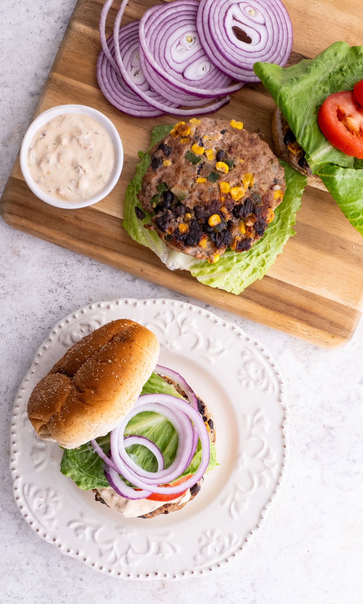 Southwest turkey burger on a plate with toppings and another burger patty and more toppings on a cutting board to the side.