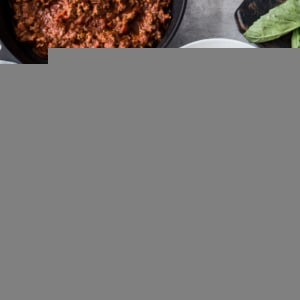 Two white bowls of spaghetti squash with red sauce on top and fresh basil leaves and a napkin to the side.