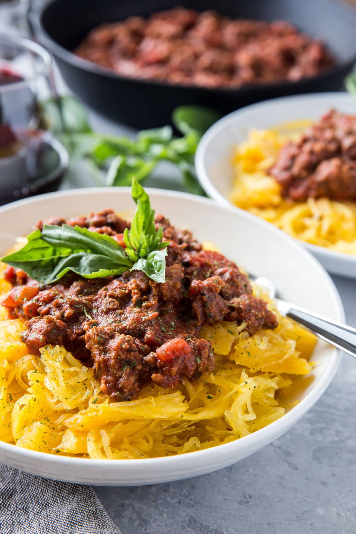 Two white bowls full of spaghetti squash and tomato based meat sauce on top, ready to serve.
