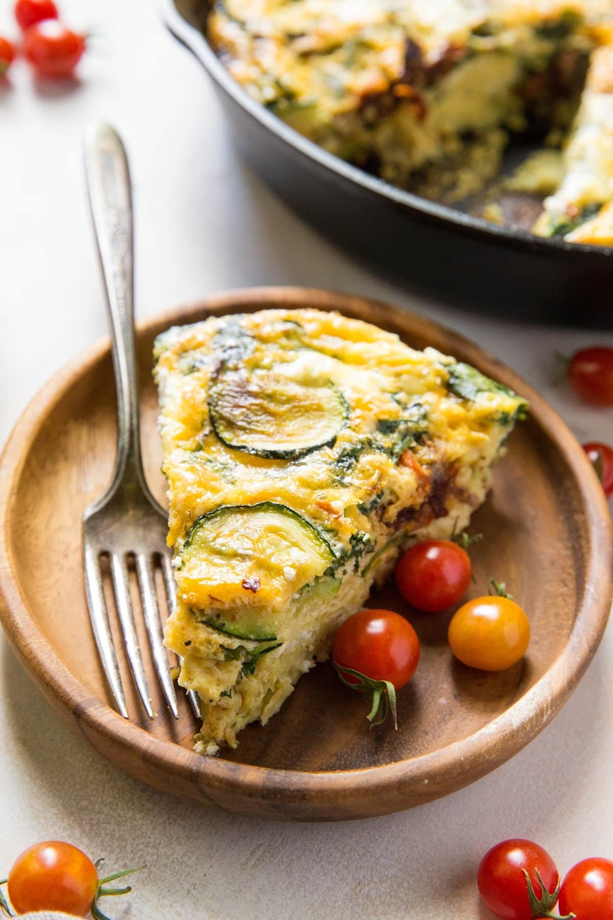 Slice of Spinach Frittata with Zucchini, Sun-Dried Tomatoes, and Goat Cheese on a plate with the rest of the frittata in the background.