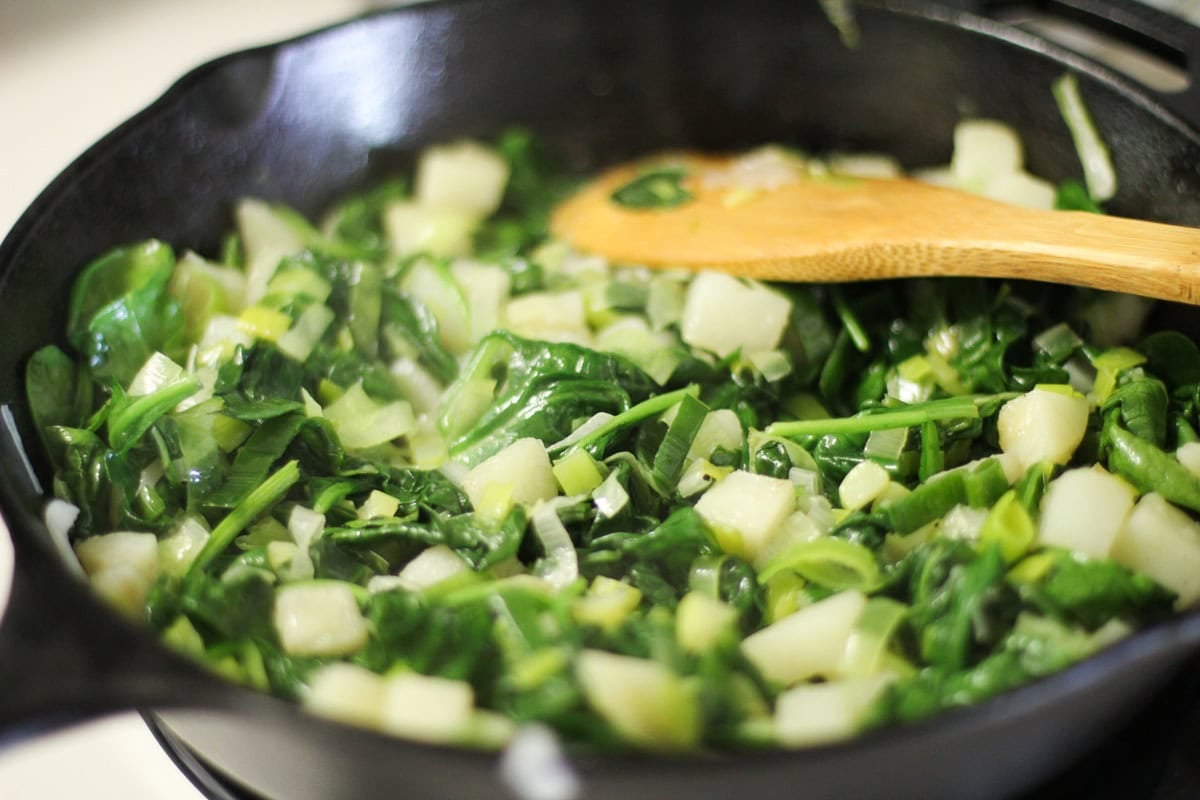 Cast iron skillet with potatoes, spinach, and leek sautéing.