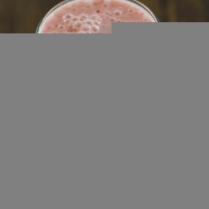 Glass of strawberry banana smoothie with a kale leaf to the side.