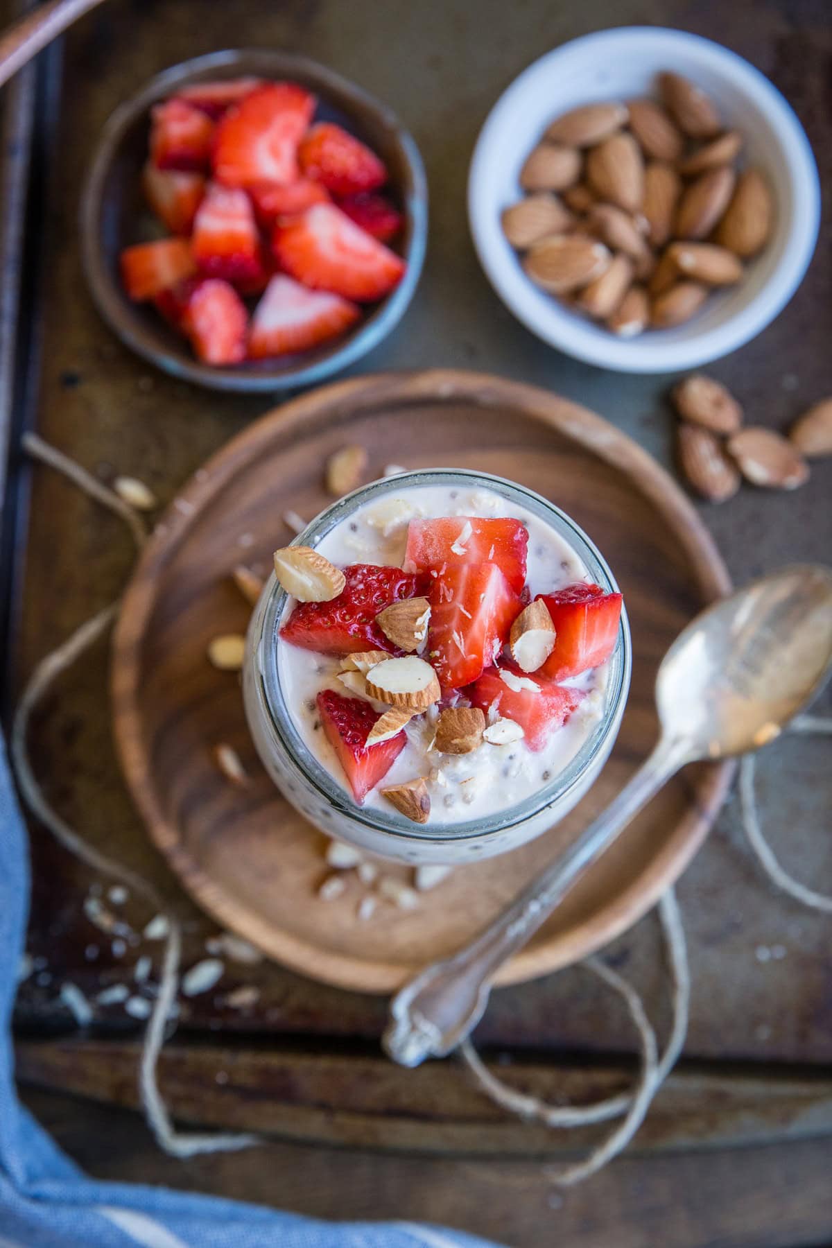 Jar full of overnight oats with chopped fresh strawberries and nuts sprinkled on top. a bowl of almonds and a bowl of fresh berries to the side.