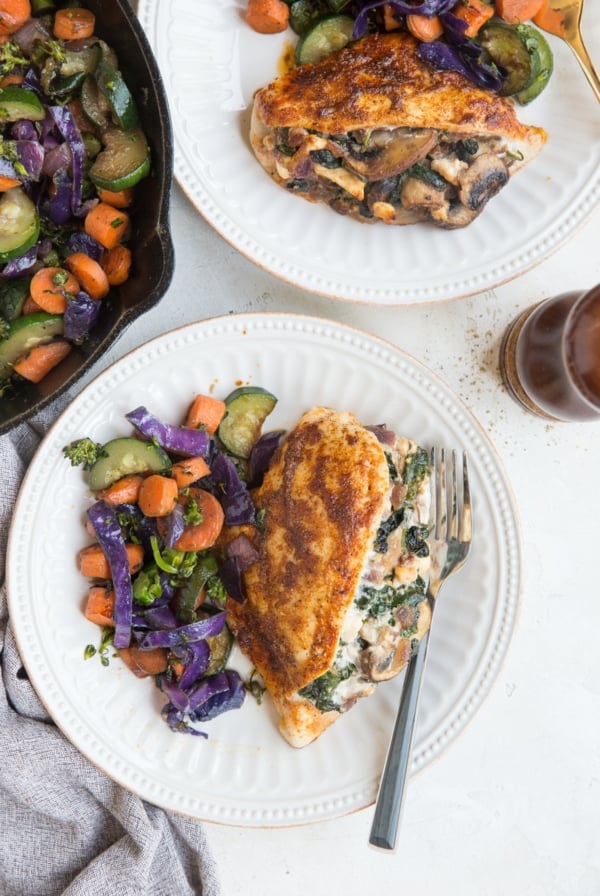 Easy Stuffed Chicken with mushrooms, spinach, onion and feta. Two plates with a stuffed breast and roasted vegetables with forks and a napkin.