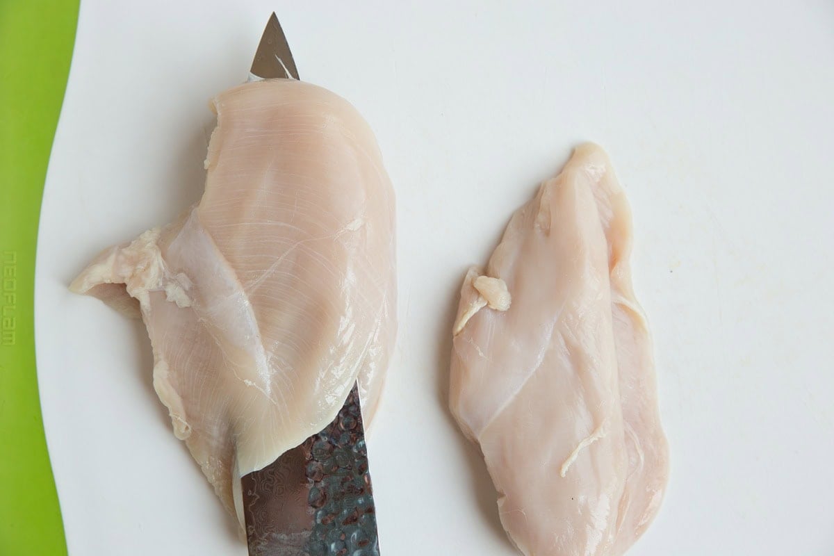 Chef's knife slicing through a chicken breast to create a pocket for stuffing.
