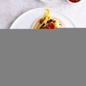 Plate of sweet potato and black bean breakfast tacos with eggs and avocado on top, ready to eat.