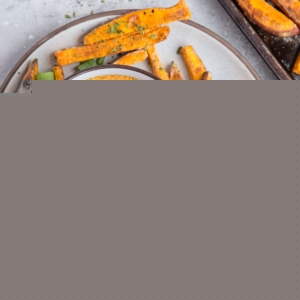 Sweet potato fries on a plate with a bowl of chipotle dipping sauce in the center, sprinkled with green onions. Ready to serve.