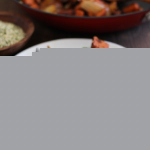 Small white plate with sweet potato home fries with fried eggs on top and sliced avocado, sprinkled with seasonings.