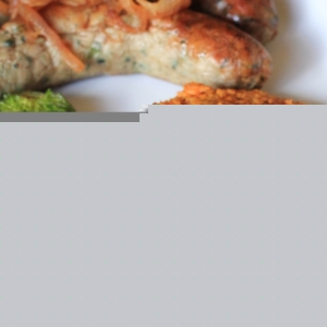 Rosti (hash browns) made with Sweet Potato on a white plate next to sauteed brussel sprouts and two sausages.