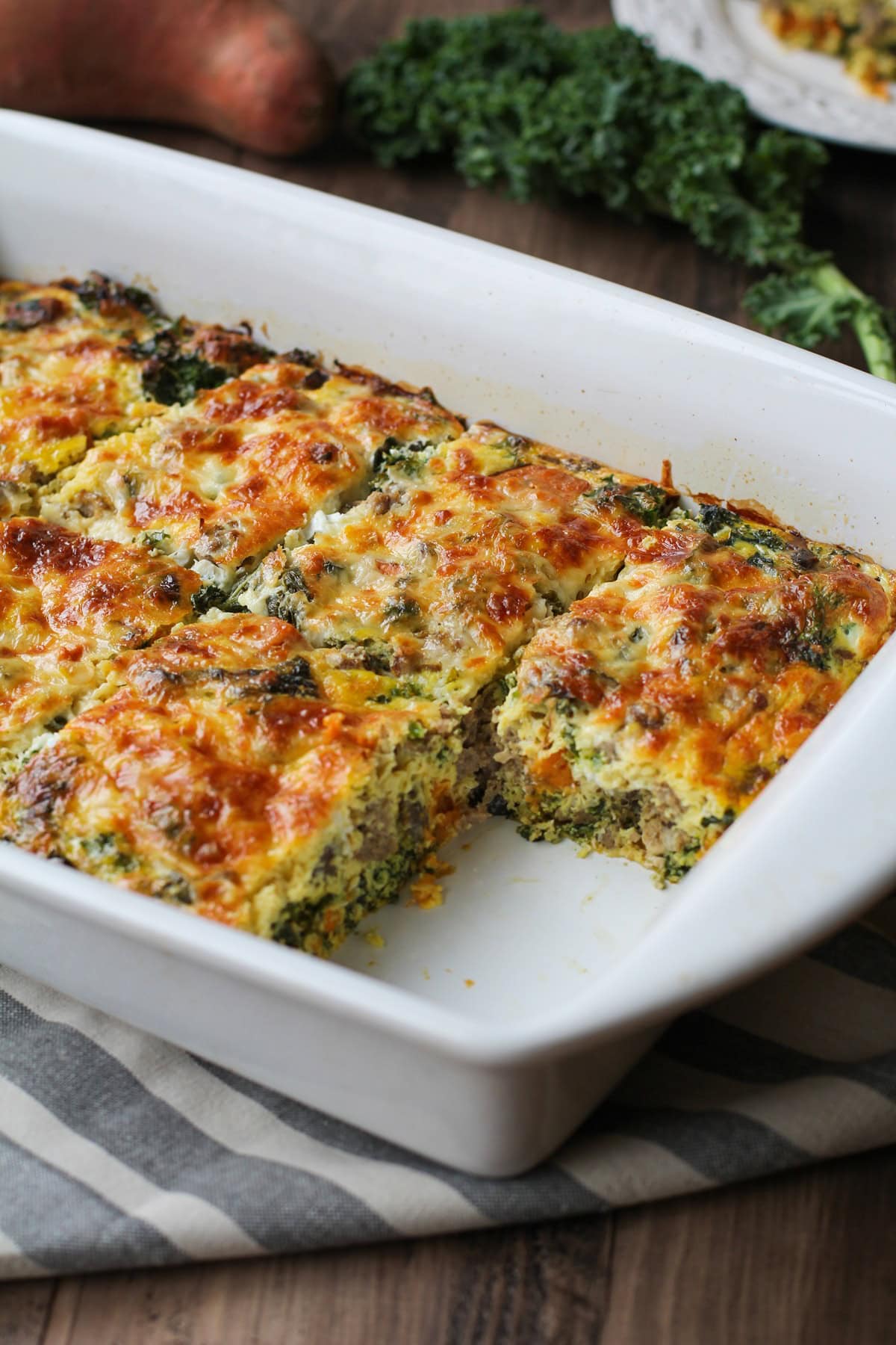 Sweet potato and sausage egg casserole in a baking dish with a piece missing, fresh out of the oven.
