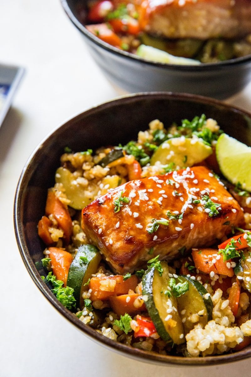 Big ceramic blue bowl full of sauteed vegetables, rice, and a teriyaki salmon filet sprinkled with sesame seeds. Ready to eat!