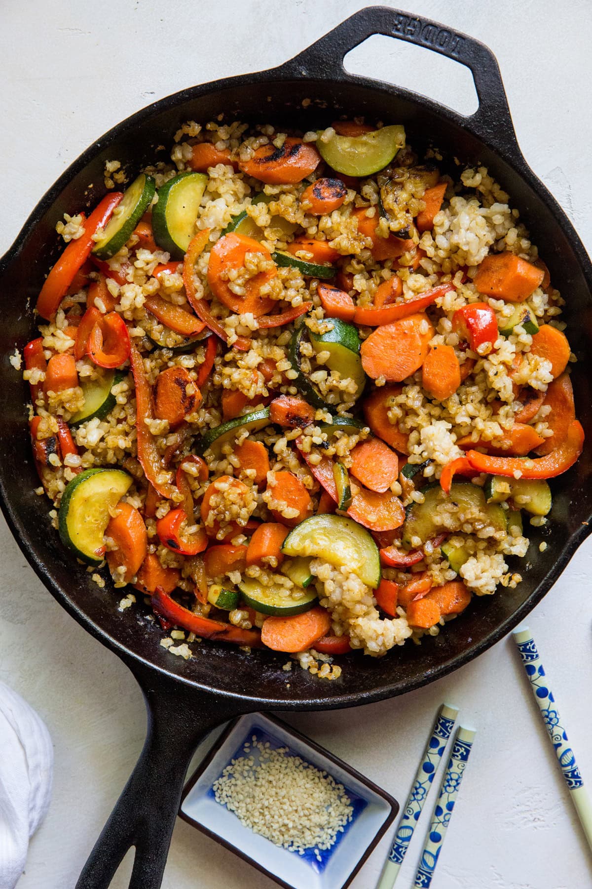 Cast iron skillet full of vegetables and rice with chopsticks to the side.