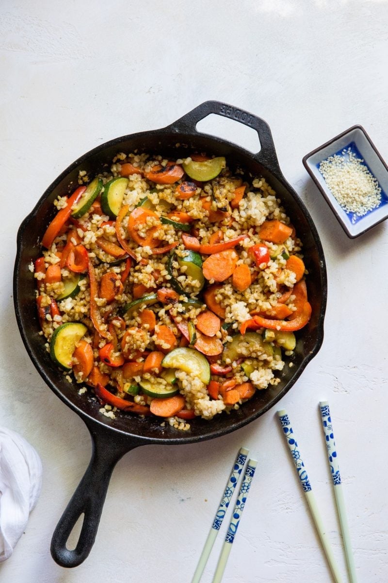 Teriyaki Stir Fry Vegetables with Rice in a cast iron skillet with two sets of chop sticks to the side.