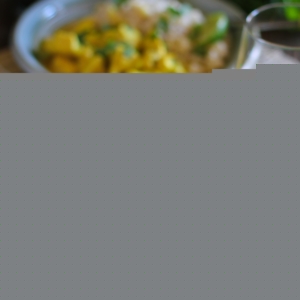 Yellow Thai curry in a bowl with brown rice and fresh limes and cilantro. on a wooden table.