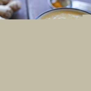 Thai Peanut Sauce in a bowl with chopsticks to the side and fresh ginger in the background.
