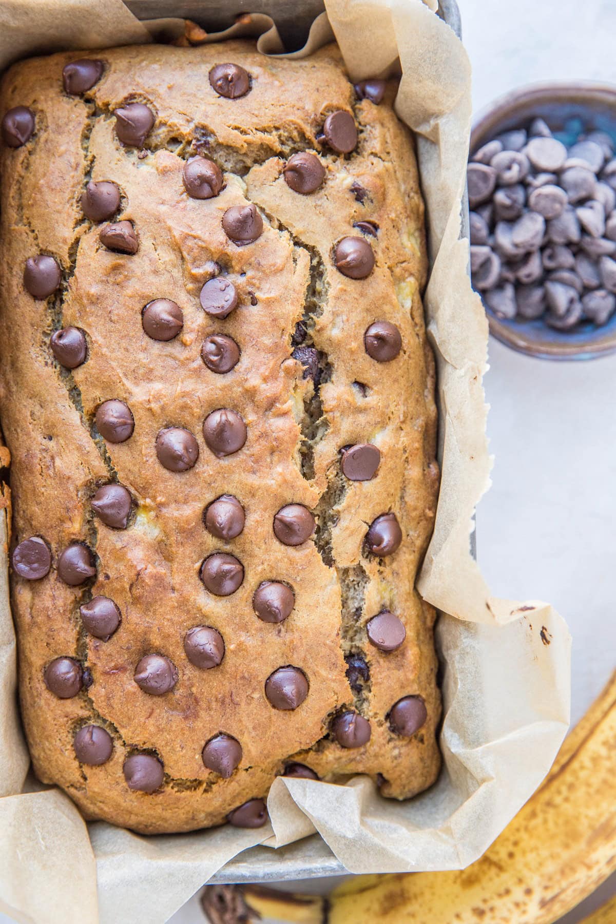 Loaf of gluten-free banana bread in a loaf pan fresh out of the oven with a ripe banana to the side.