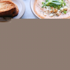 Creamy Vegan Tomato Basil Soup in two bowls with fresh basil on top and a cream colored napkin to the side.