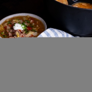 Sausage and cabbage stew in two bowls with a pot of soup in the background