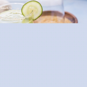 Two glasses of avocado cocktail on a blue surface with fresh mint leaves all around.