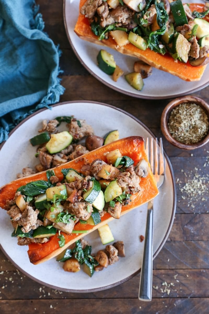 Two halves of butternut squash on two plates, stuffed with ground turkey, kale, mushrooms, zucchini, and more. Ready to serve.