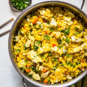 Turmeric Chicken Fried Rice in a stainless steel skillet with a green napkin to the side and a bowl full of chopped green onions.