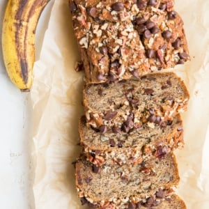Loaf of vegan banana bread cut into individual slices with fresh ripe bananas to the side.