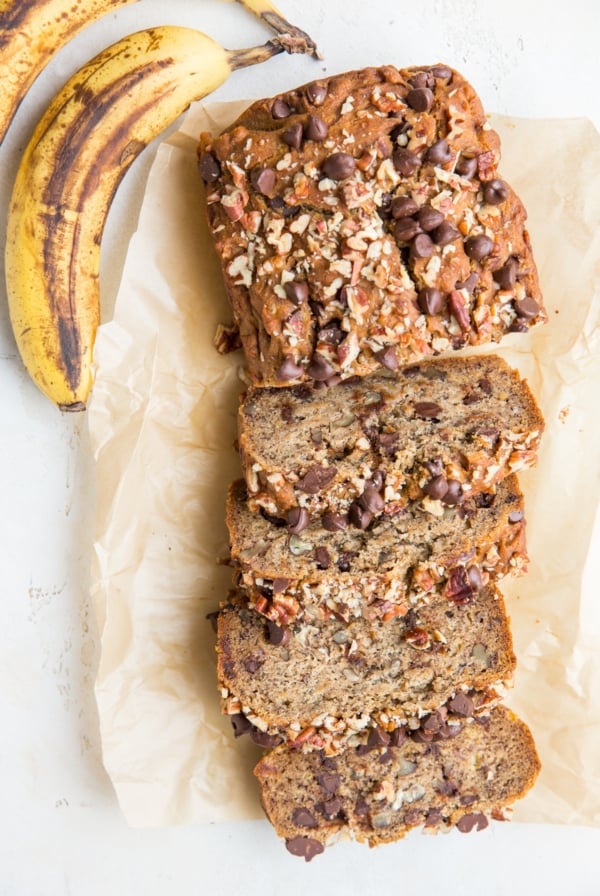 Loaf of vegan banana bread cut into individual slices with fresh ripe bananas to the side.