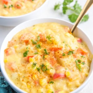 Two big white bowls full of vegan corn chowder, sprinkled with fresh chopped parsley and a dark blue napkin to the side.