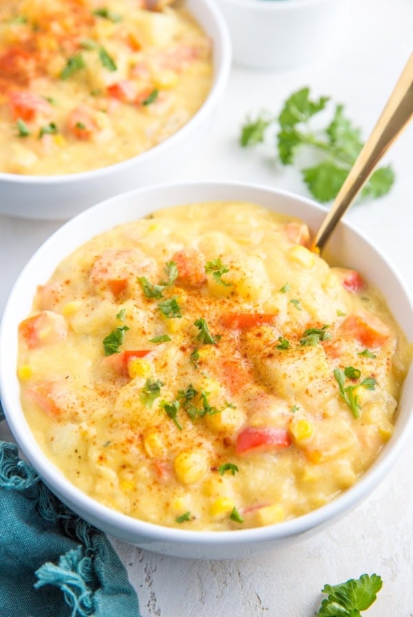 Two big white bowls full of vegan corn chowder, sprinkled with fresh chopped parsley and a dark blue napkin to the side.