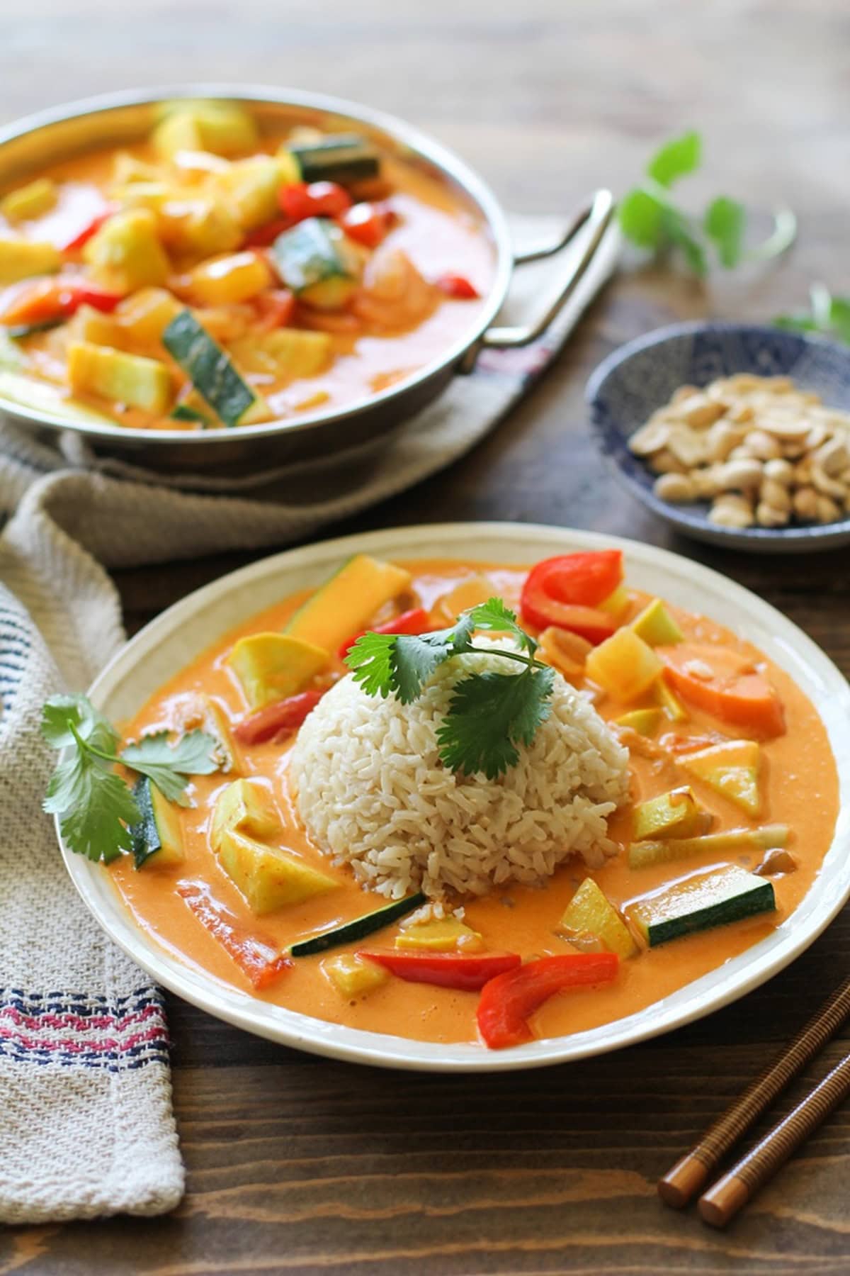 Vegetable curry in a white bowl with brown rice in the middle and fresh cilantro on top. Chopsticks and a napkin to the side.