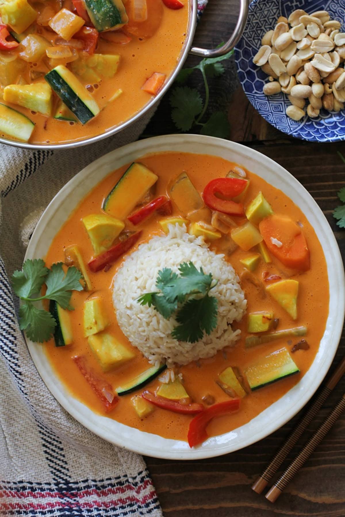 Two shallow bowls with red vegetable curry and scoops of brown rice in the center. Chopsticks and napkin to the side.