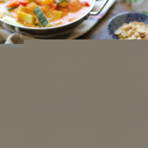 Bowl of vegetable red curry with a scoop of rice in the middle sitting on a wood table with chop sticks and a burlap napkin.