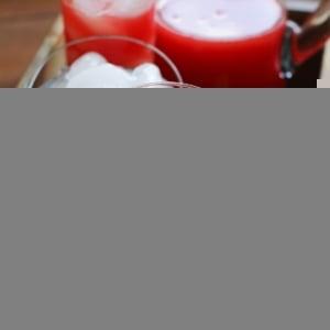 Wooden tray with two glasses and a pitcher of pink Watermelon Agua Fresca with ice and a floral napkin. Ready to serve.