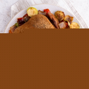 Whole smoked chicken on a plate on top of roasted vegetables, fresh off the smoker grill and ready to serve.