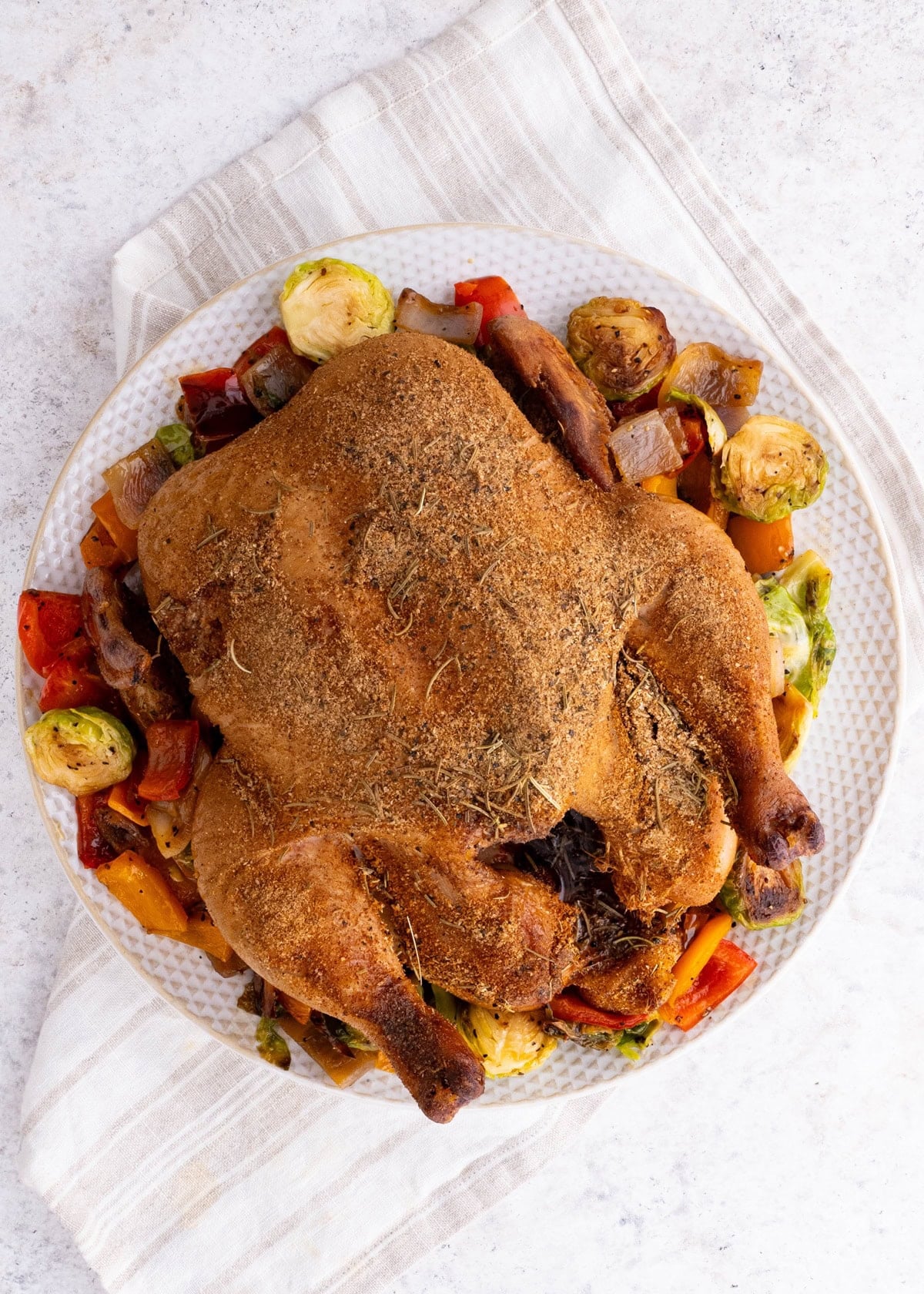 Whole smoked chicken on a plate on top of roasted vegetables, fresh off the smoker grill and ready to serve.